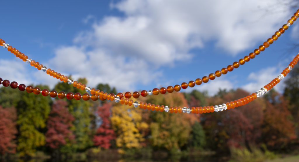 Two Carnelian gemstone necklaces with sky and trees in background.