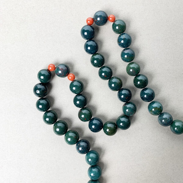 Green necklace with Bloodstone and Red Coral gemstones on white surface.
