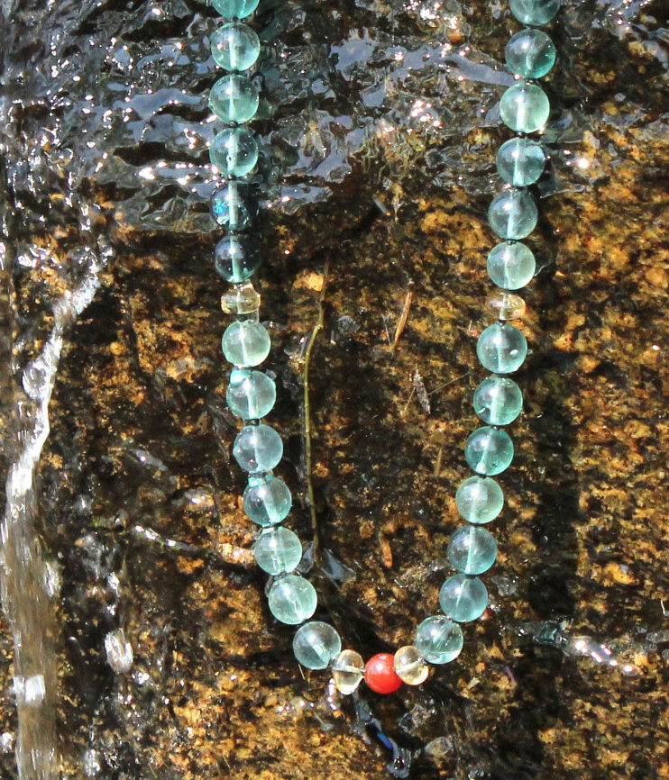 Blue-green Fluorite gemstone necklace against rock